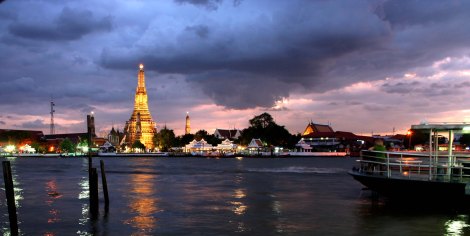 The sun sets over Chao Phraya River in Bangkok, Thailand just behind Wat Arun, the Temple of Dawn